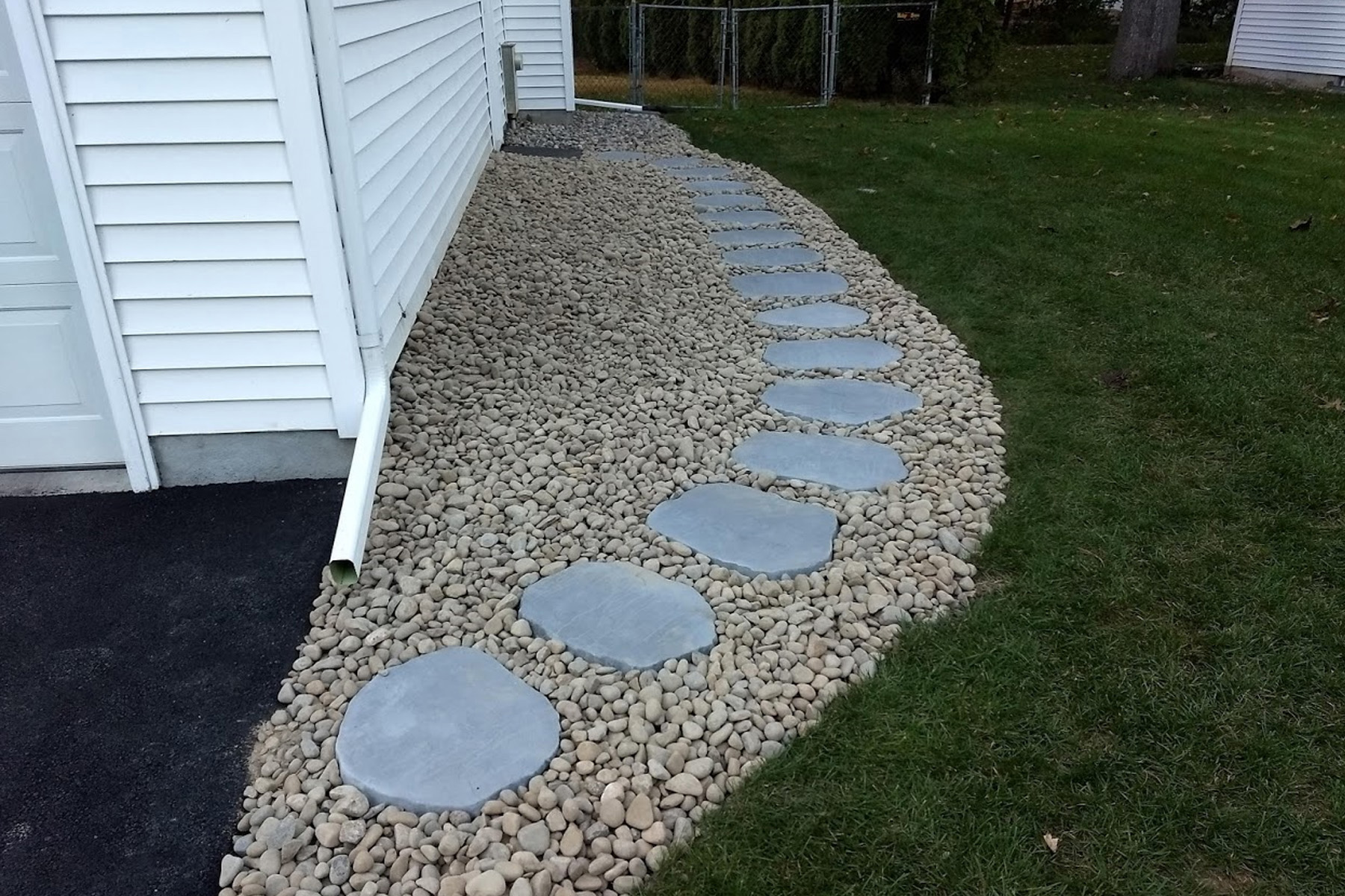 Thumbnail of the completed paver path with smooth lanscaping rocks surrounding the pavers along the side of the garage