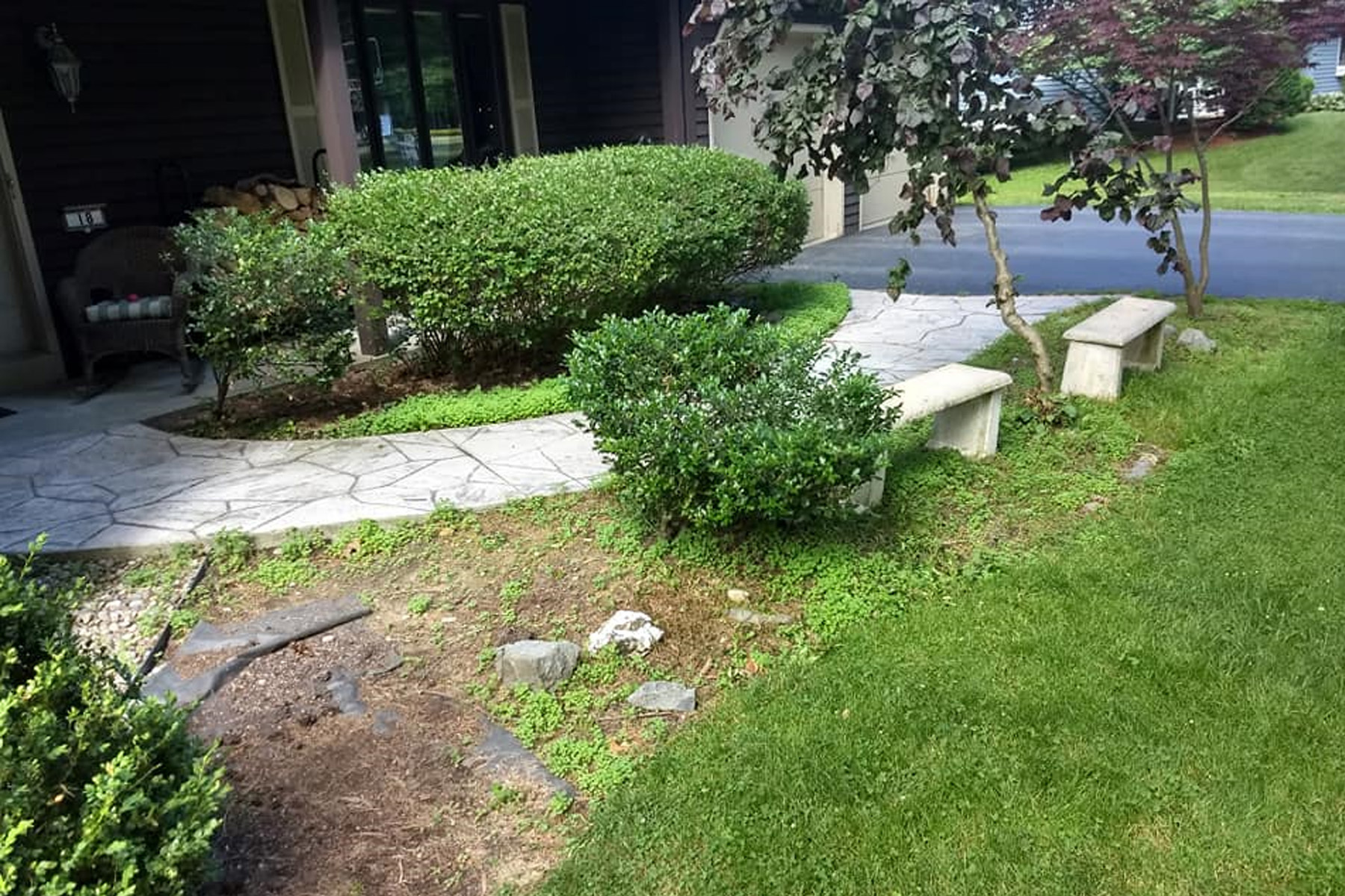 Thumbnail of an overgrown plant bed and stone seating area in the front of a house